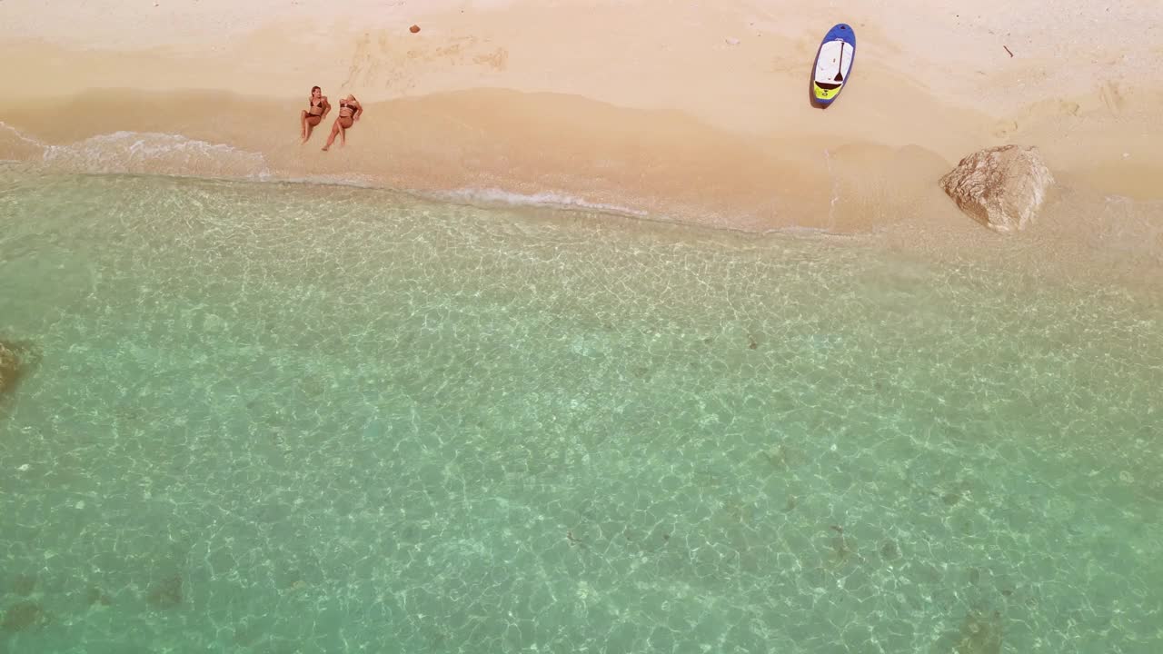 两个美丽的年轻女子在海滩上放松和日光浴。鸟瞰图视频素材