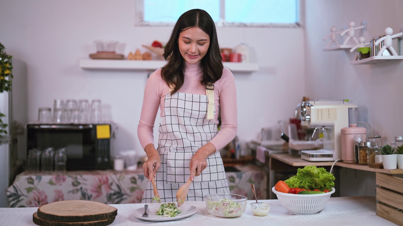 年轻健康的亚洲妇女微笑的家庭主妇准备健康的膳食素食健康吃新鲜蔬菜沙拉在厨房。视频素材