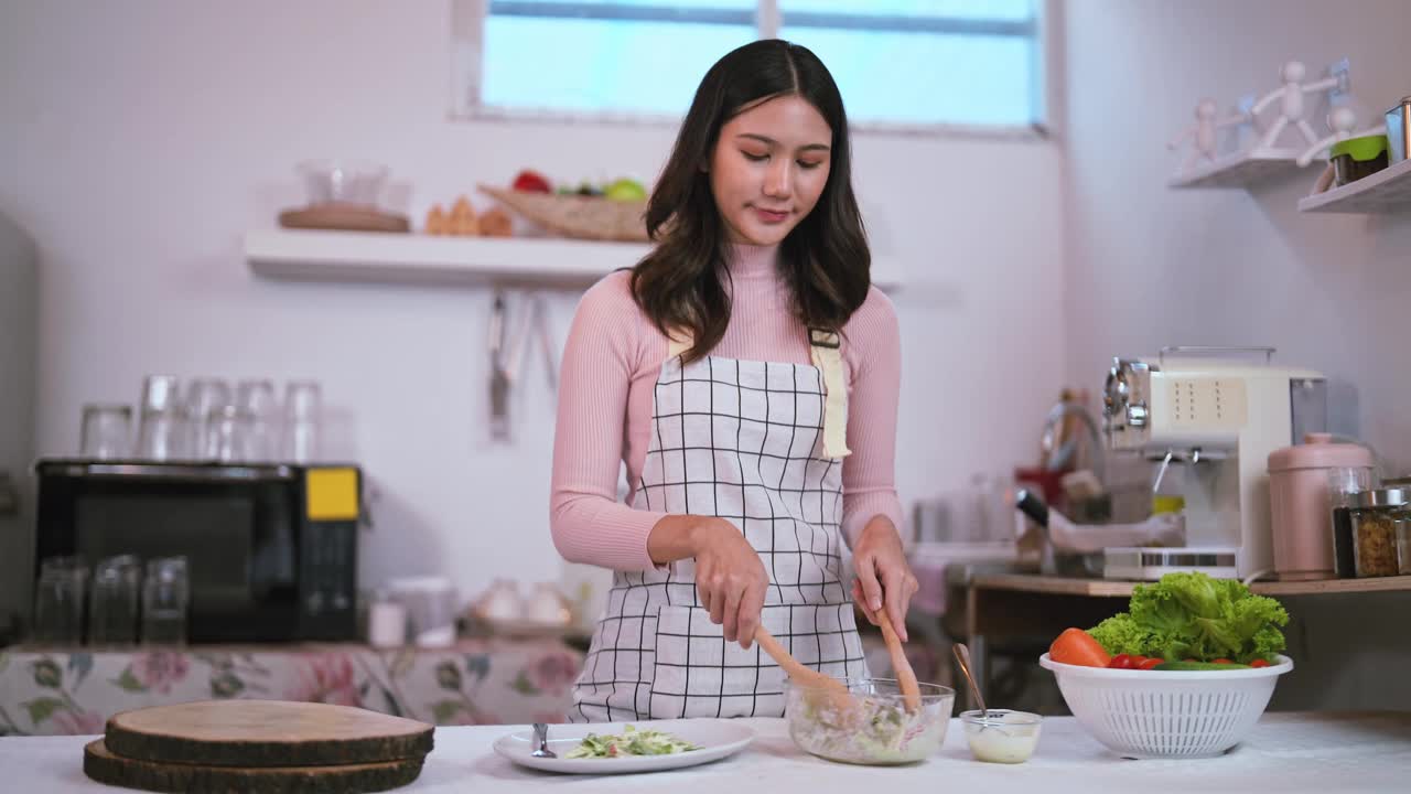 年轻健康的亚洲妇女微笑的家庭主妇准备健康的膳食素食健康吃新鲜蔬菜沙拉在厨房。视频素材