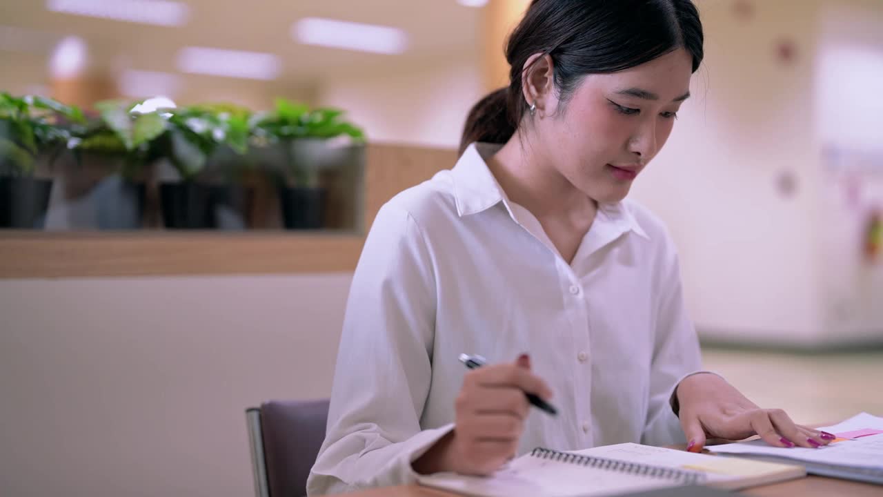 年轻的亚洲女大学生在图书馆做作业和读期末考试的书，教育理念。视频素材