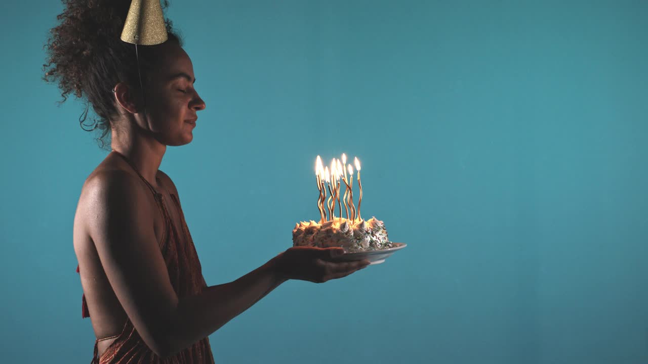 年轻女子在蓝色背景下吹灭生日蛋糕上的蜡烛视频素材