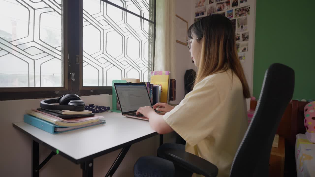 年轻的女学生在她的房间里用笔记本电脑学习视频素材