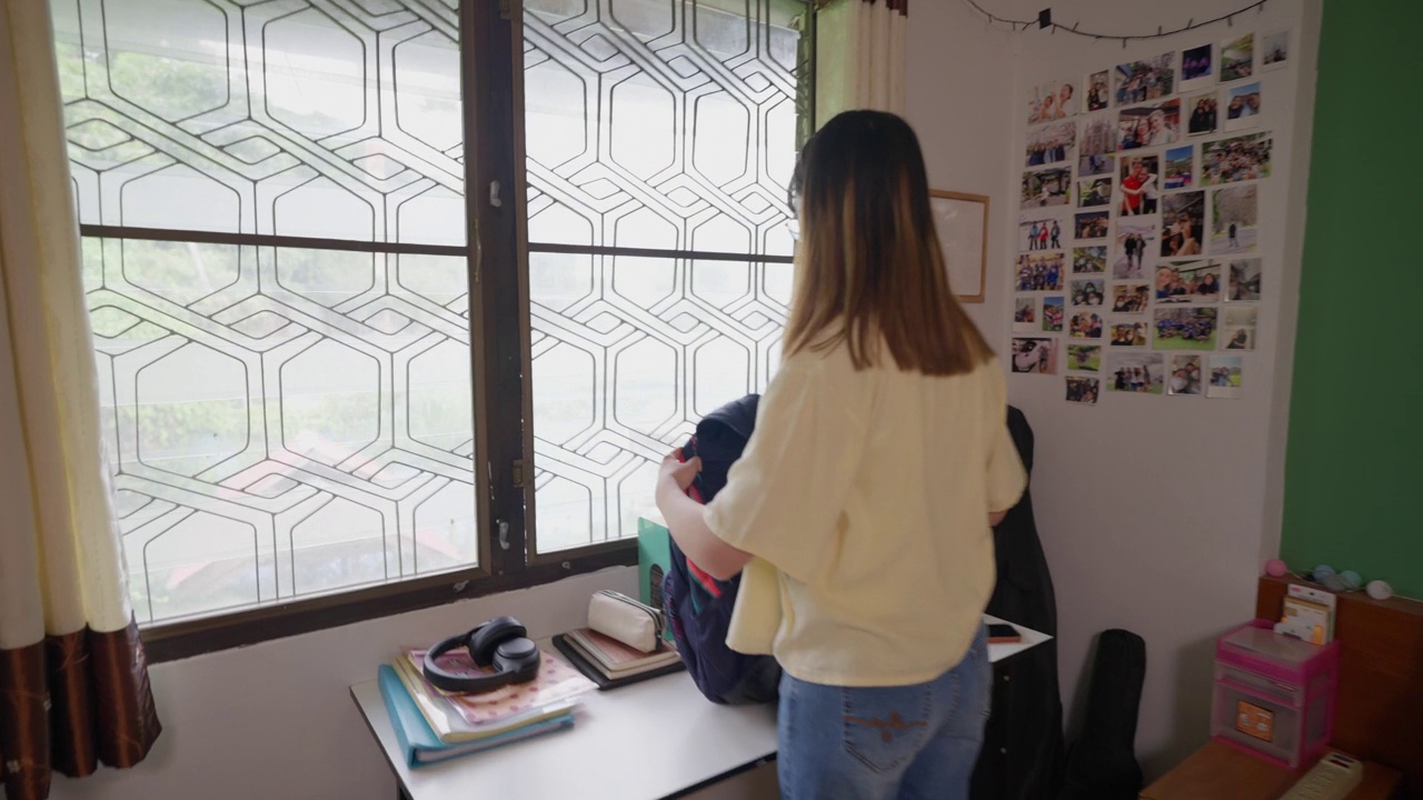 年轻的女学生在她的房间里，上学前把学习材料放进书包里视频素材