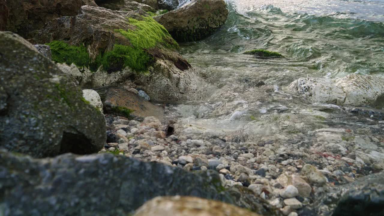 海浪在海滩上翻滚，拍打着岩石和悬崖，海藻和藻类不断生长。美丽的风景，自然背景，海洋背景视频素材