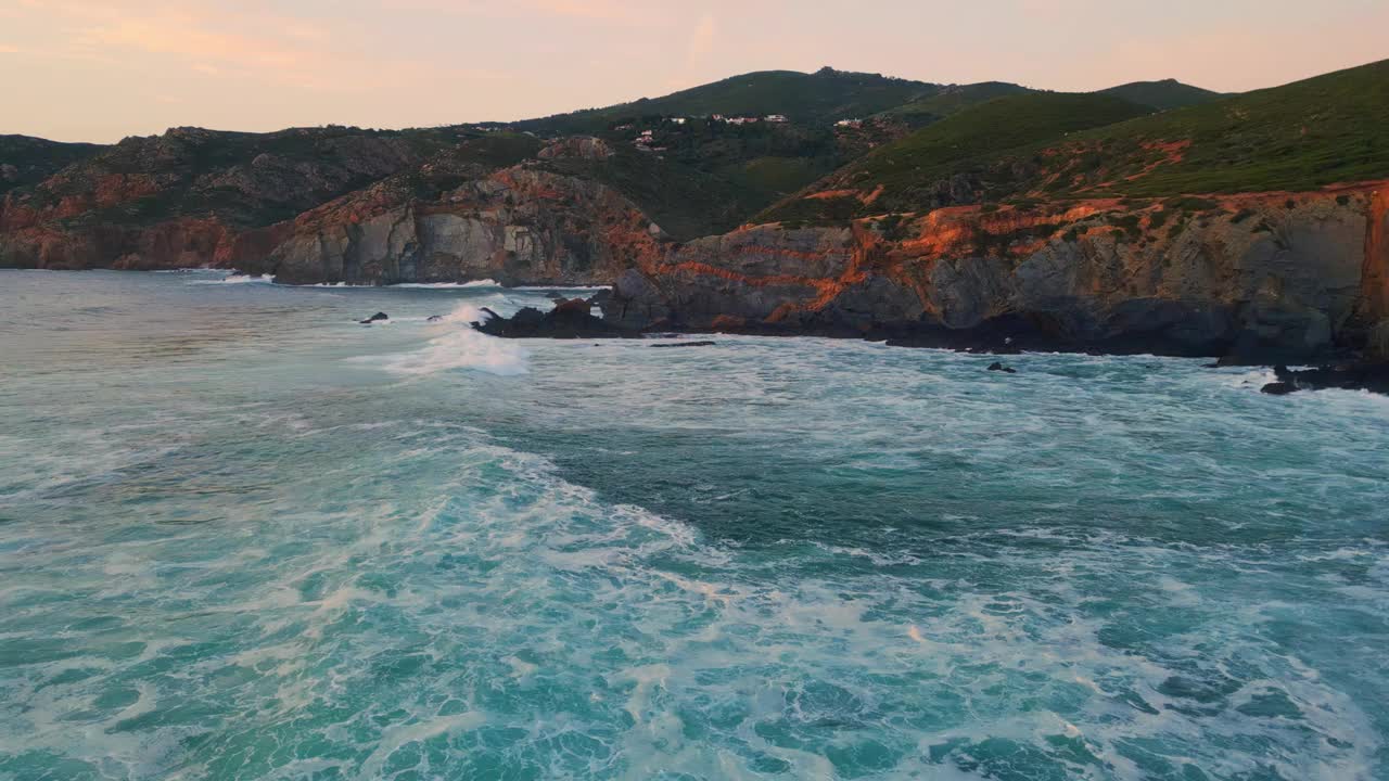 傍晚岩石山景观航拍。波涛汹涌的海水拍打着粗糙的岩石峭壁视频素材