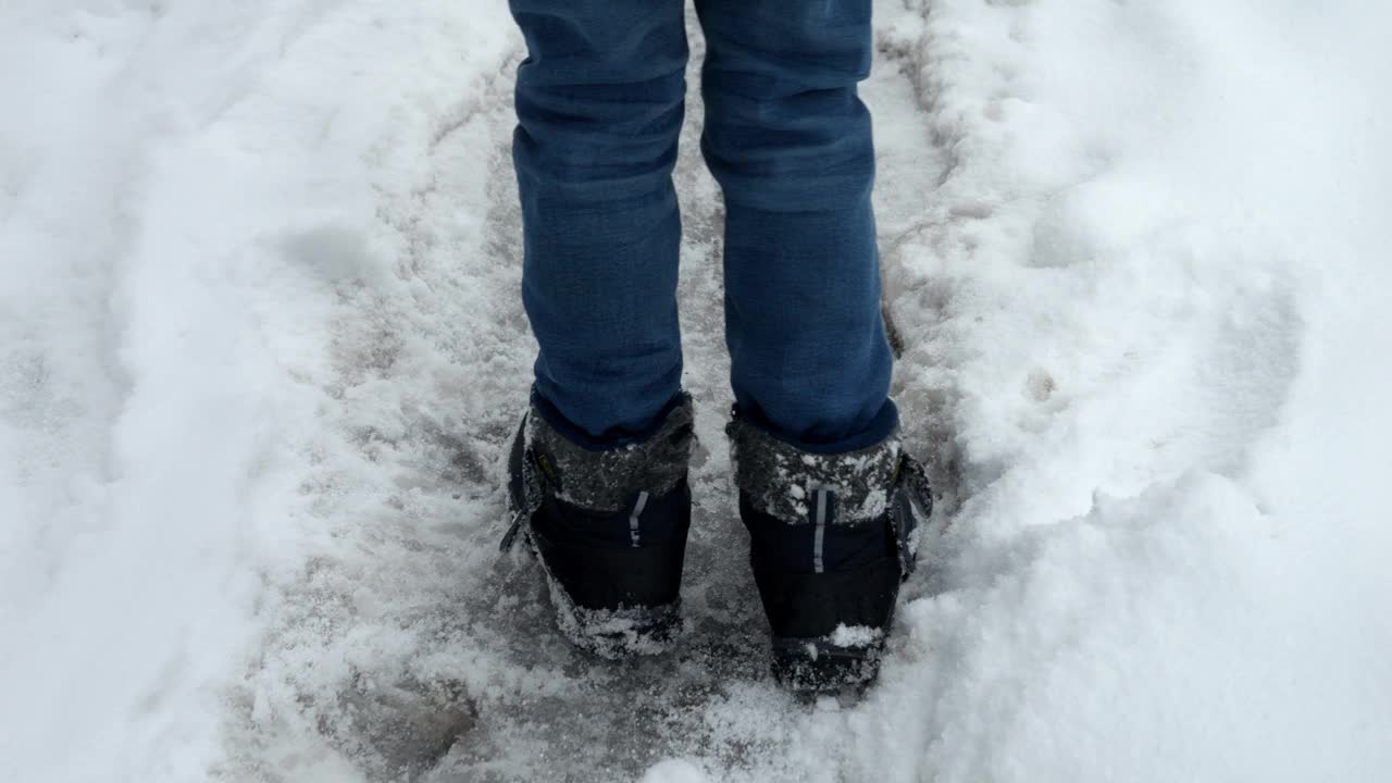 暴风雪过后，孩子穿着雪地靴走在被雪覆盖的路上。视频素材