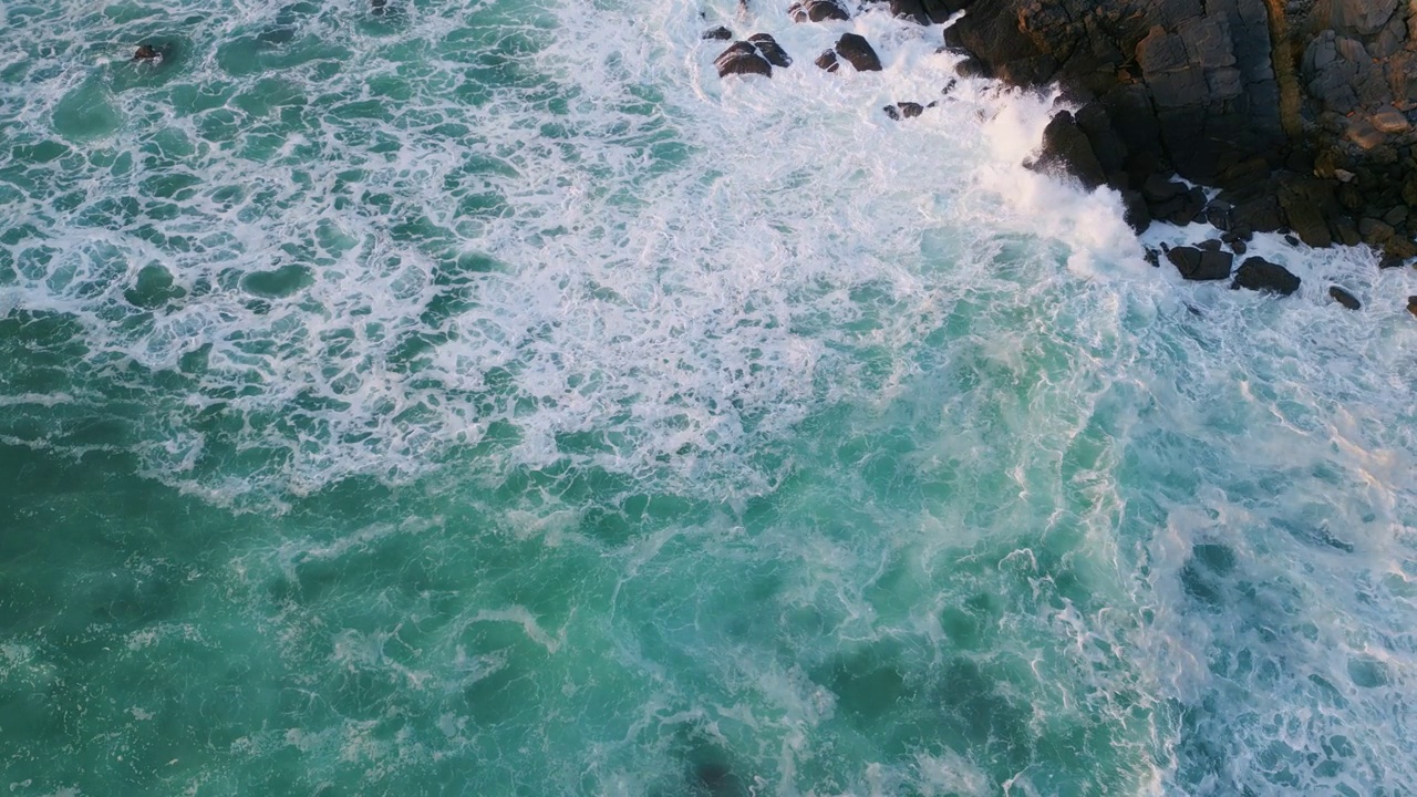 泡沫般的波浪拍打着岩石。飞溅的海浪覆盖着黑色的悬崖视频素材