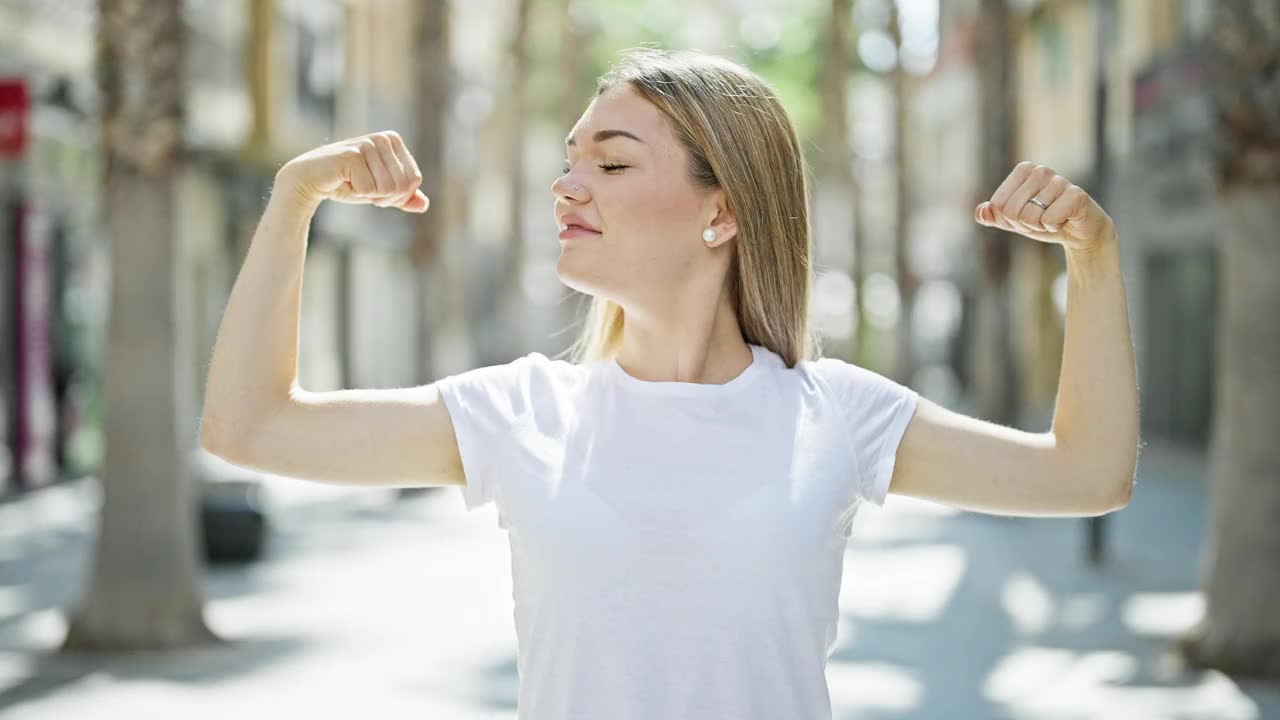 年轻的金发女子微笑着自信地在街上做着有力的手势视频素材