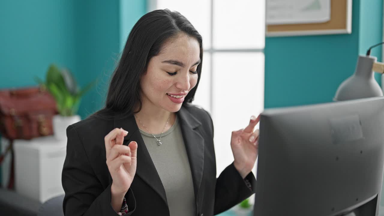 年轻漂亮的西班牙女商务工作者使用电脑交叉手指祈求好运在办公室庆祝视频素材