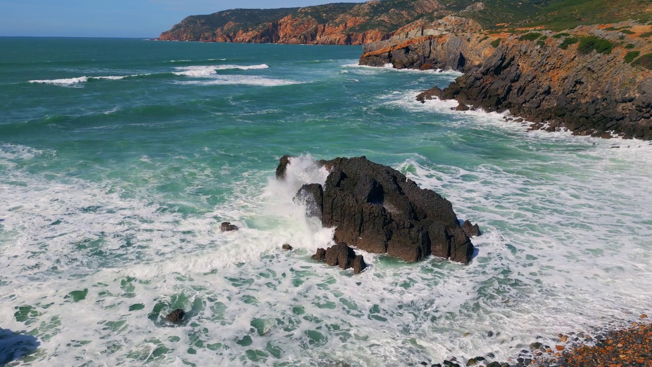 阳光明媚的日子里，汹涌的海水拍打在海岸的岩石上。无人驾驶岩石海岸线视频素材