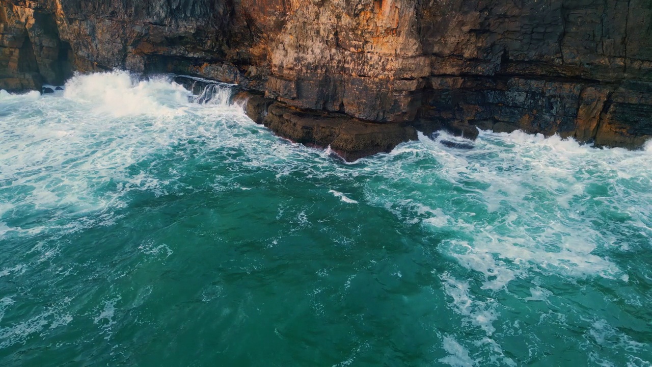 泡沫般的海浪缓慢地冲刷着岩石般的海岸线。空中暗色海岸悬崖视频素材