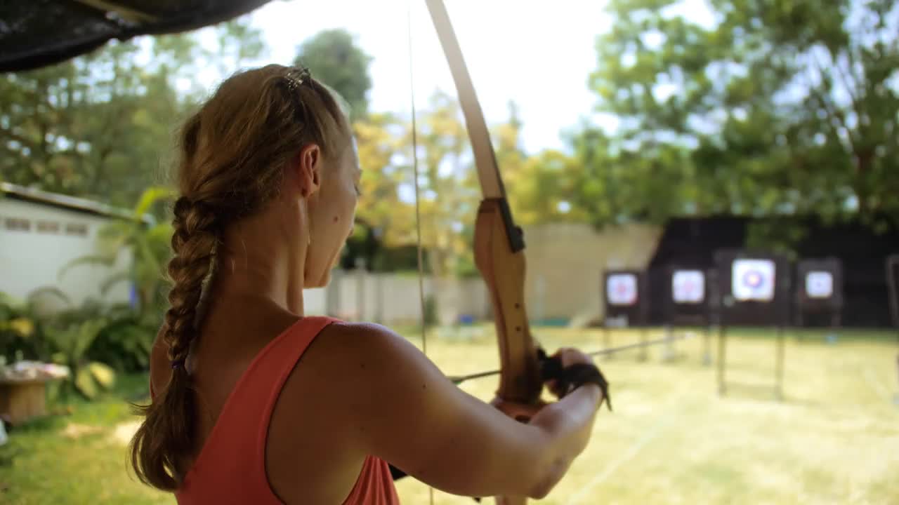 女子在射击场拿着弓。泰国游客户外娱乐场所。在射击场练习射箭。假期积极休闲，到亚洲旅游。木弓，箭命中目标。视频素材