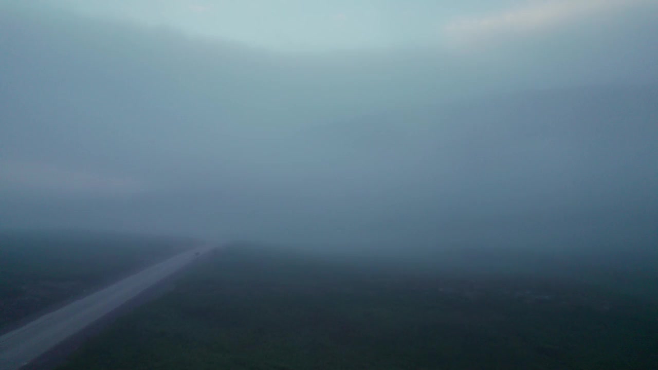 飞过低垂的浓雾，飞过一条通往山的偏僻道路视频素材