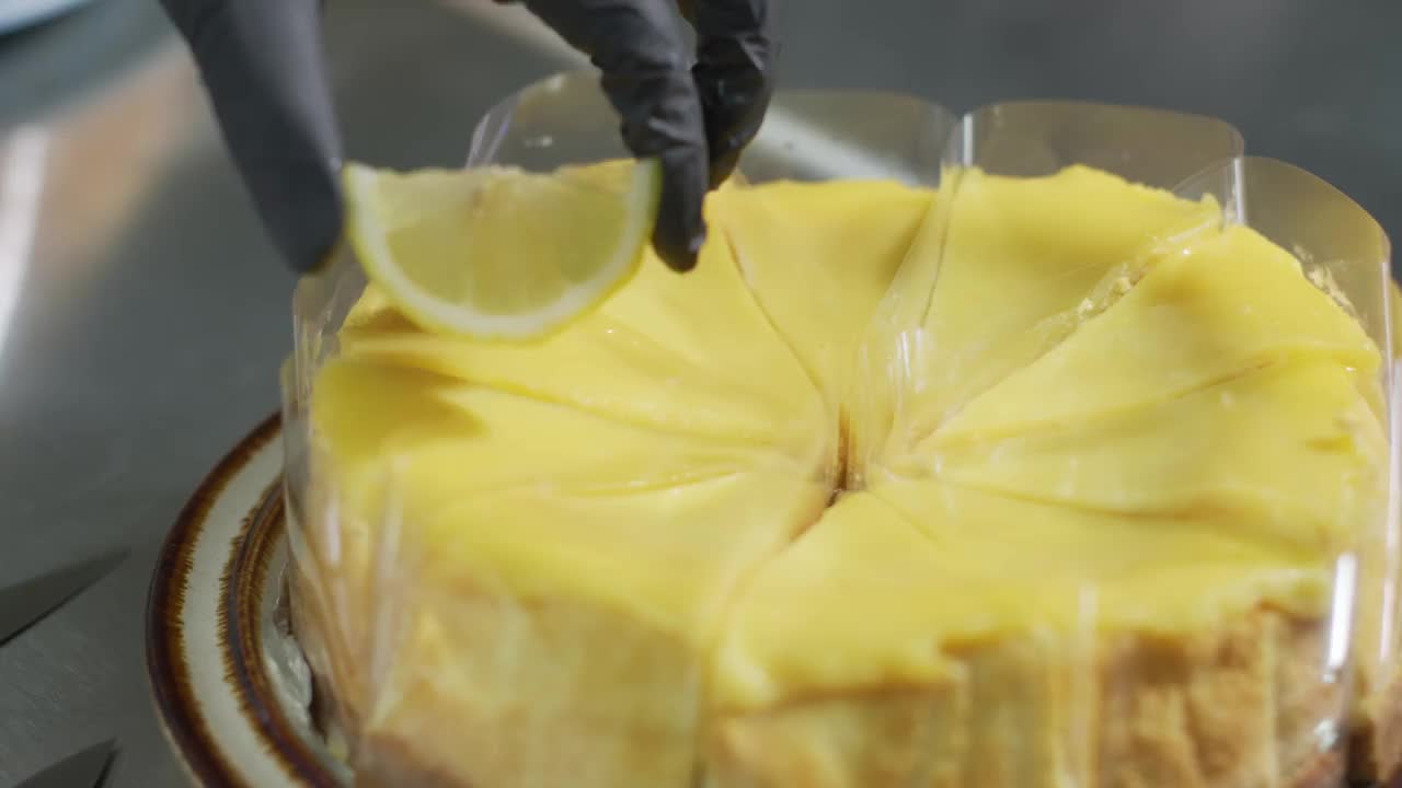 厨师戴着黑色手套的手正把柠檬片圈在柠檬凝乳蛋糕上。装饰蛋糕。在家里厨房里制作柠檬蛋糕甜点的过程。面包店视频素材