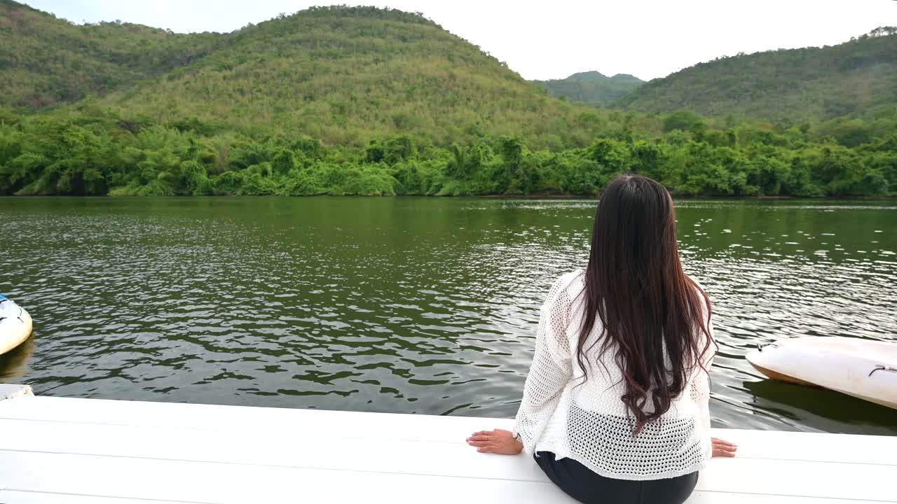 一位穿着白色衣服的亚洲年轻女子在西沙瓦特区度假时舒适地坐在河边。北视频下载