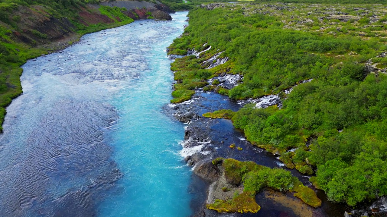 无人机拍摄的冰岛Hraunfossar瀑布景观，有绿色的山丘和流动的河流视频素材