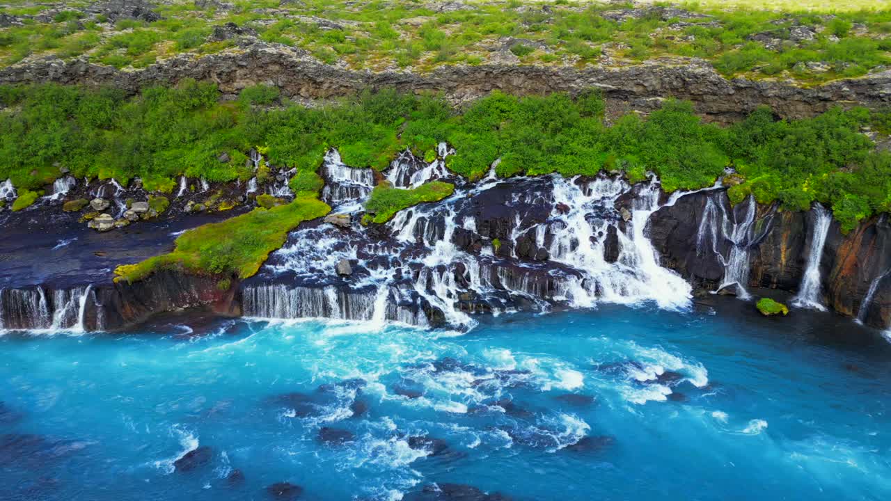 冰岛Hraunfossar瀑布景观与绿色山丘的航拍镜头视频素材