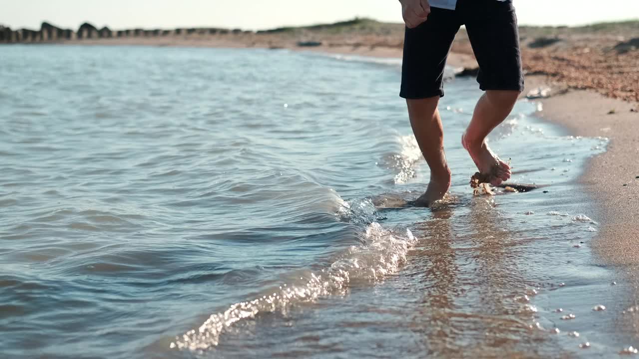 一个快乐的少年光着脚沿着海边奔跑，溅起水来。视频素材