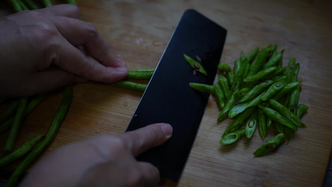 慢动作视频展示了在厨房的木制砧板上切一码长的豆子。视频素材