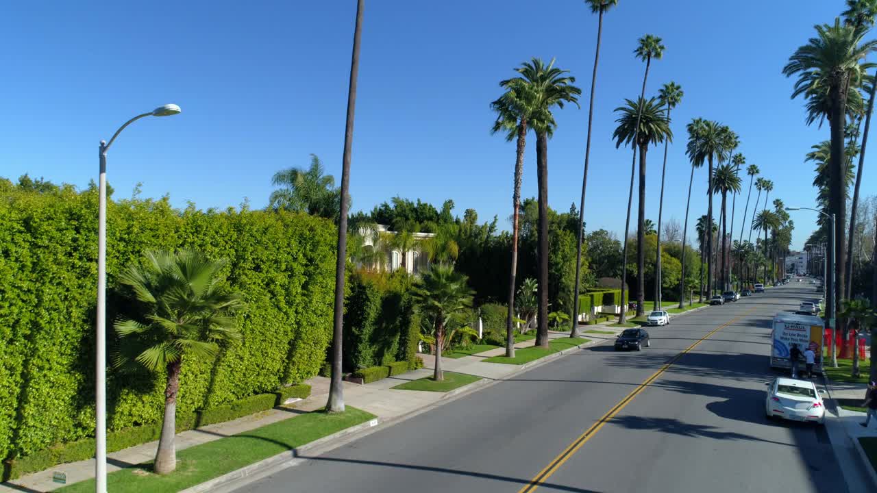 航拍拍摄的车辆在道路上的树木和房屋，无人机上升在城市的郊区对蓝天-洛杉矶，加利福尼亚视频素材