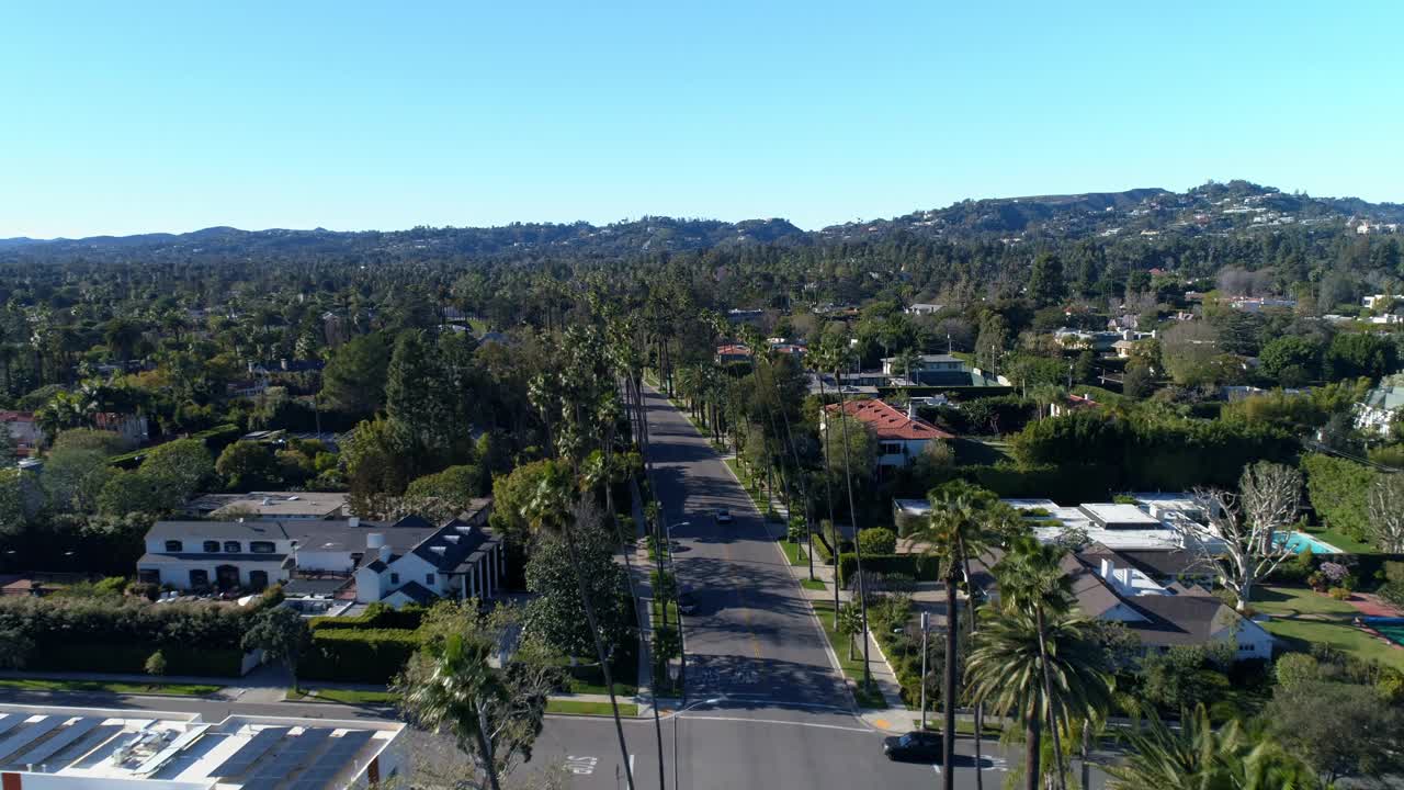 在天空湛蓝的洛杉矶附近，汽车在树木和房屋之间的道路上的鸟瞰图视频素材