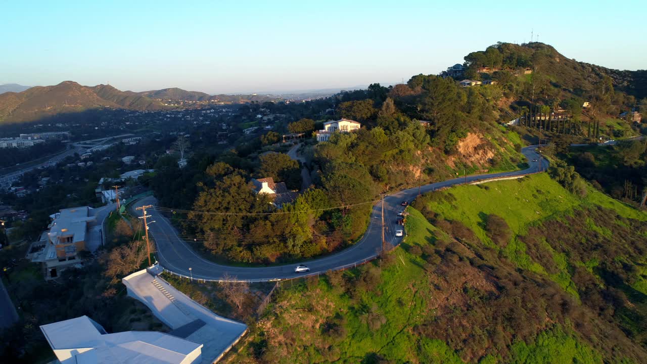 空中下降向前拍摄的车辆在蜿蜒的道路越过山对天空在日落-洛杉矶，加利福尼亚视频素材