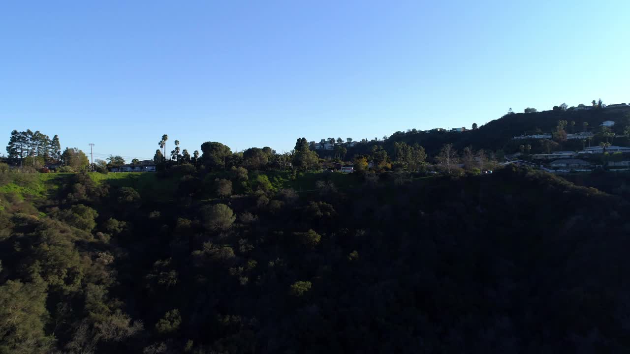 空中向前拍摄的房屋和车辆在树木和植物在山上对蓝天-洛杉矶，加利福尼亚视频素材