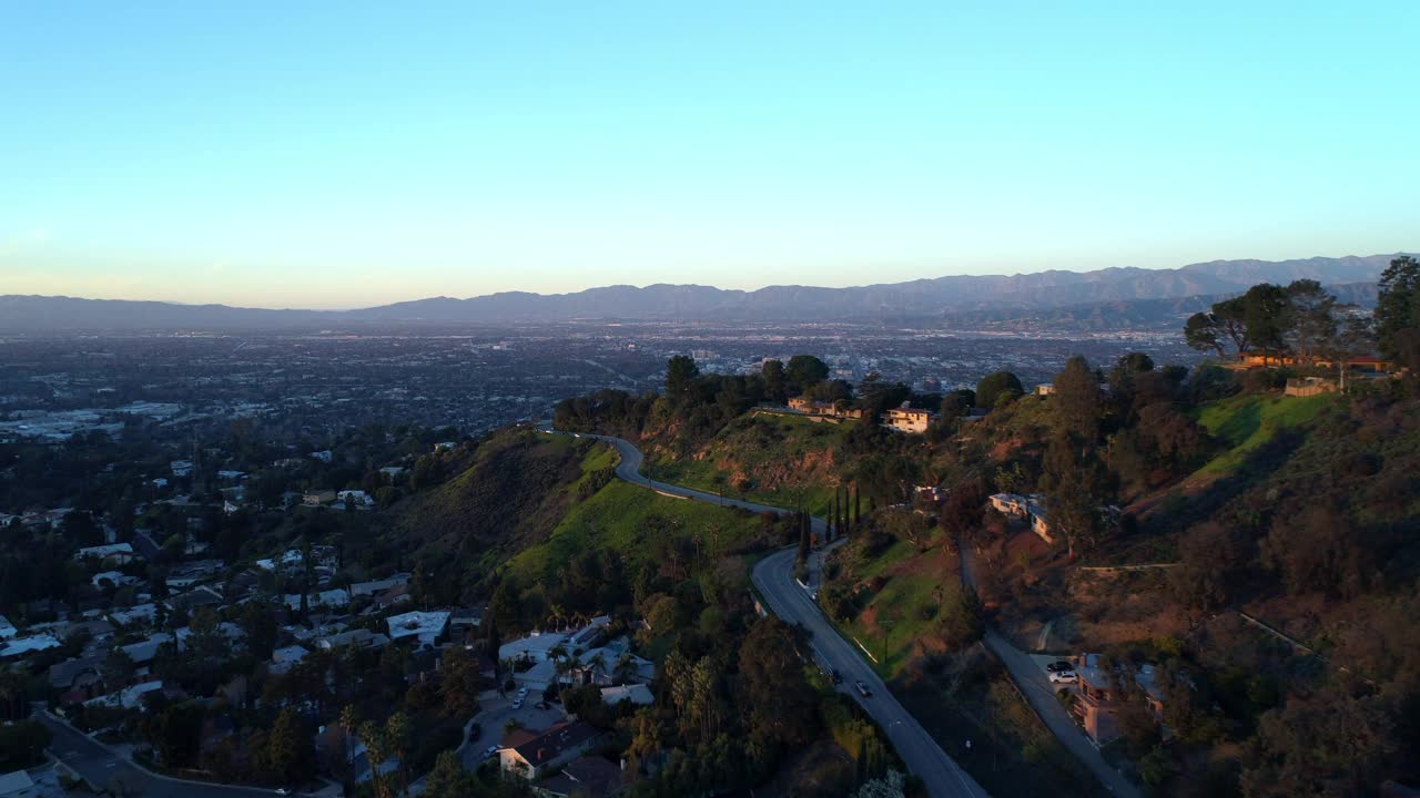 空中下降向前拍摄蜿蜒的道路在山上与房屋对天空在日落-洛杉矶，加利福尼亚视频素材