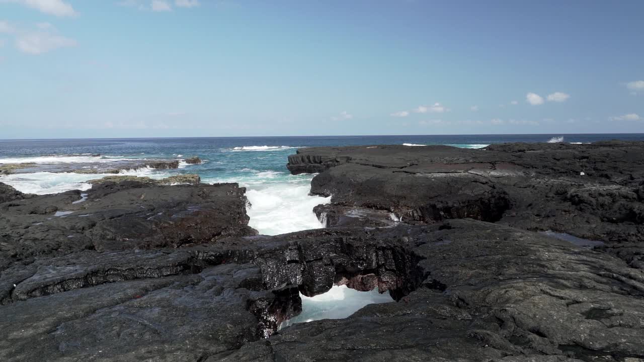 在一个阳光明媚的日子里，深蓝色的太平洋海浪冲击着加拉帕戈斯群岛的黑色火山熔岩。视频素材