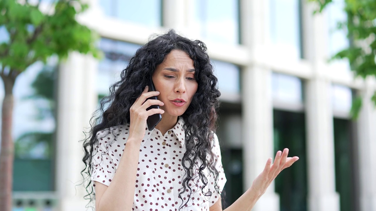 愤怒的年轻女员工站在办公楼附近的街道上用智能手机争吵视频素材