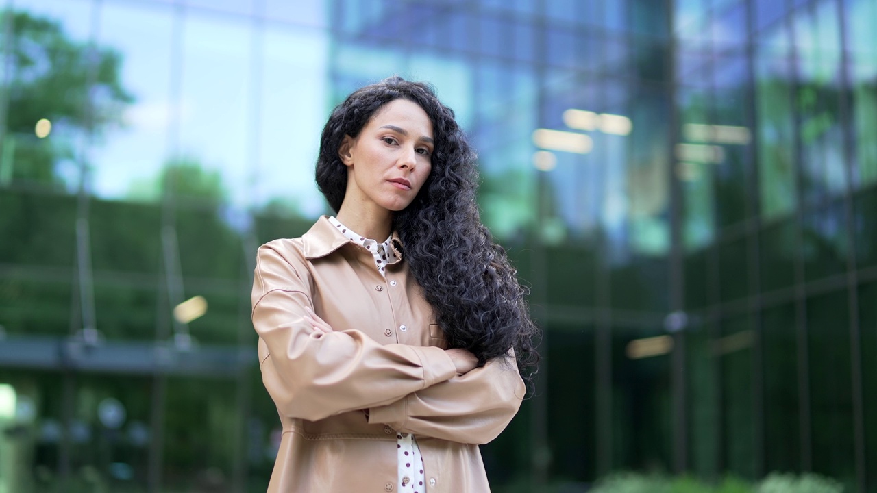 一个严肃的年轻女商人的肖像，双臂交叉站在办公楼附近的街道上视频素材