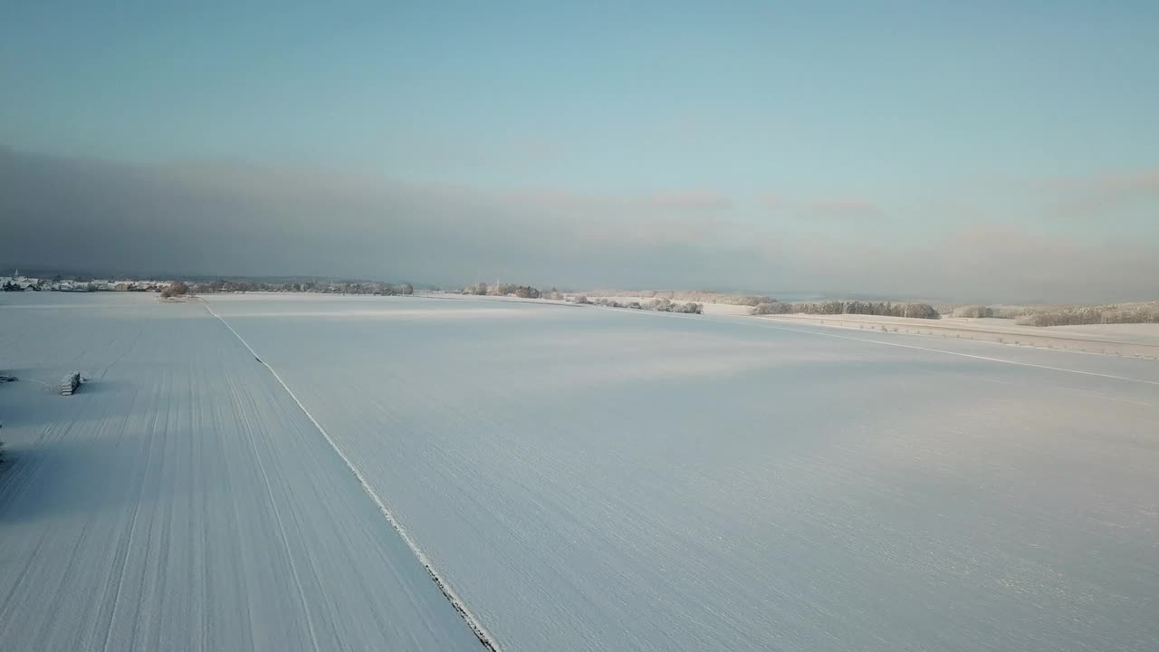 鸟瞰图，白雪覆盖的田野和乡村房屋，明亮的天空在地平线上视频素材