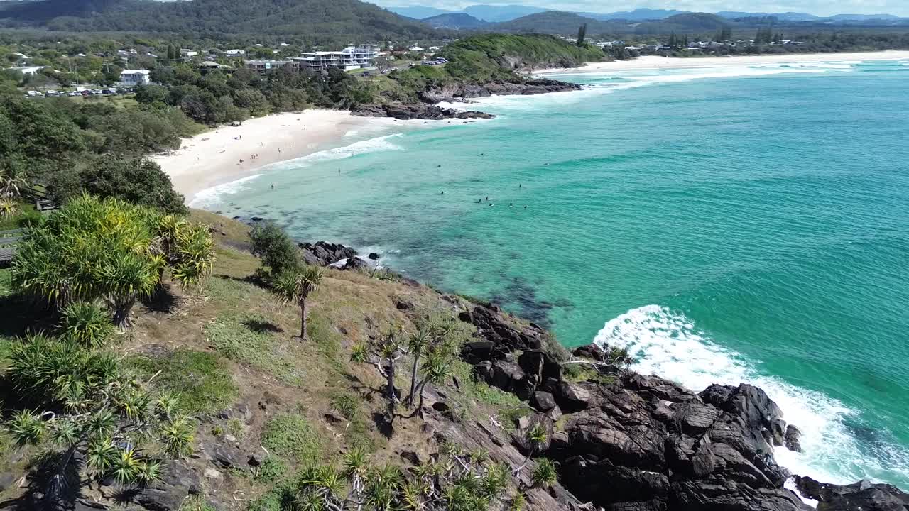 无人机飞过悬崖，一群人在它后面靠近海滩的海面上冲浪视频素材