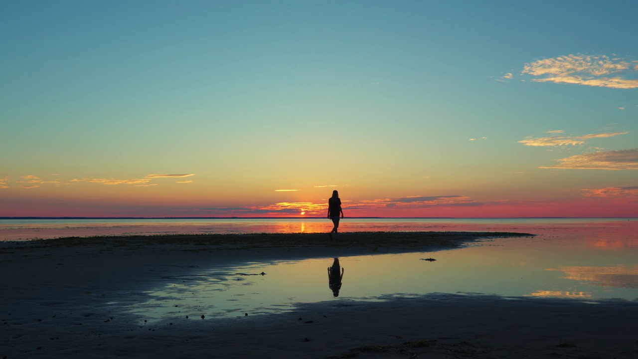 浪漫的女孩走在海岸上，粉红色和绿松石色的夕阳和太阳落在地平线上视频素材