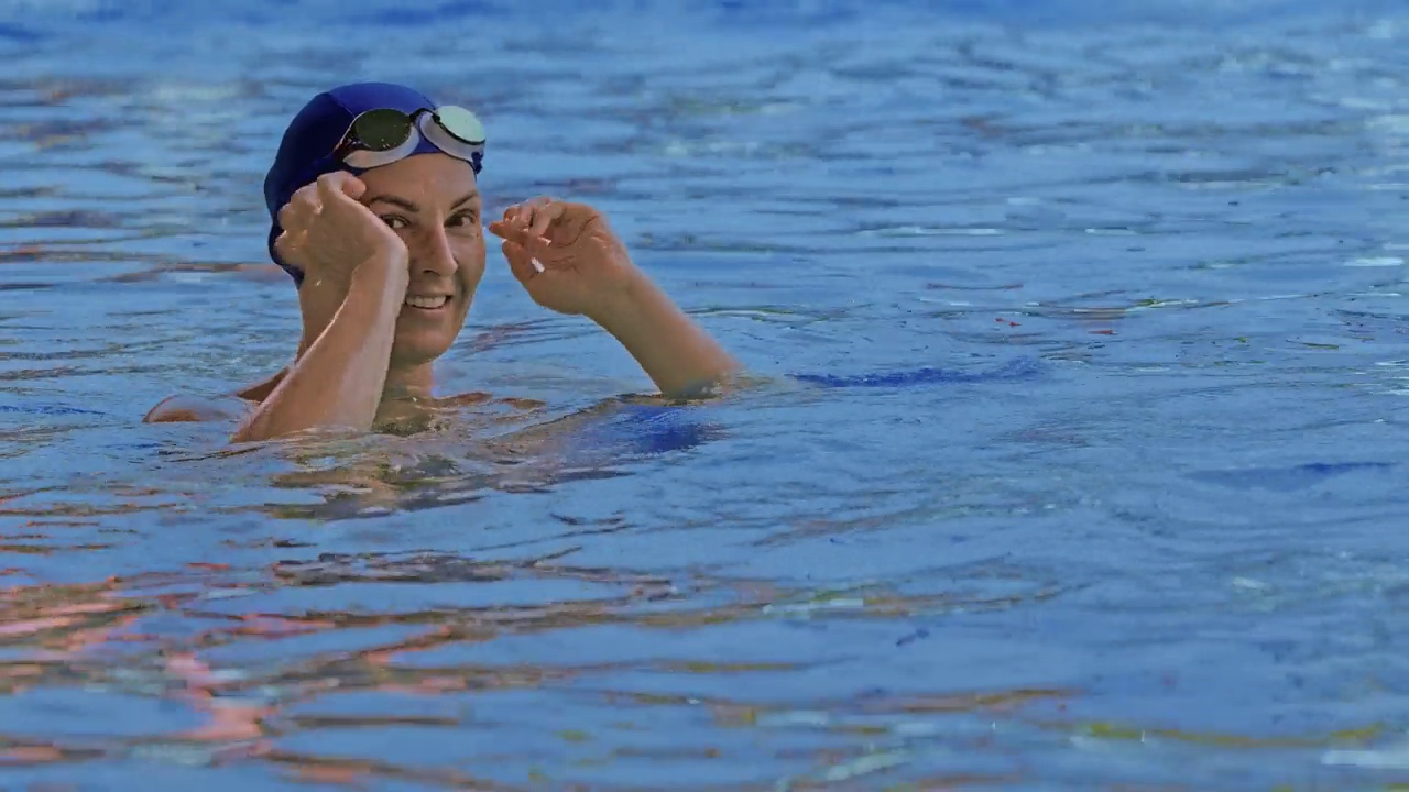 泳池边戴着护目镜的专业游泳运动员的正面视图。一位女游泳运动员调整了眼镜，开始在镜头前训练游泳。特写镜头视频下载