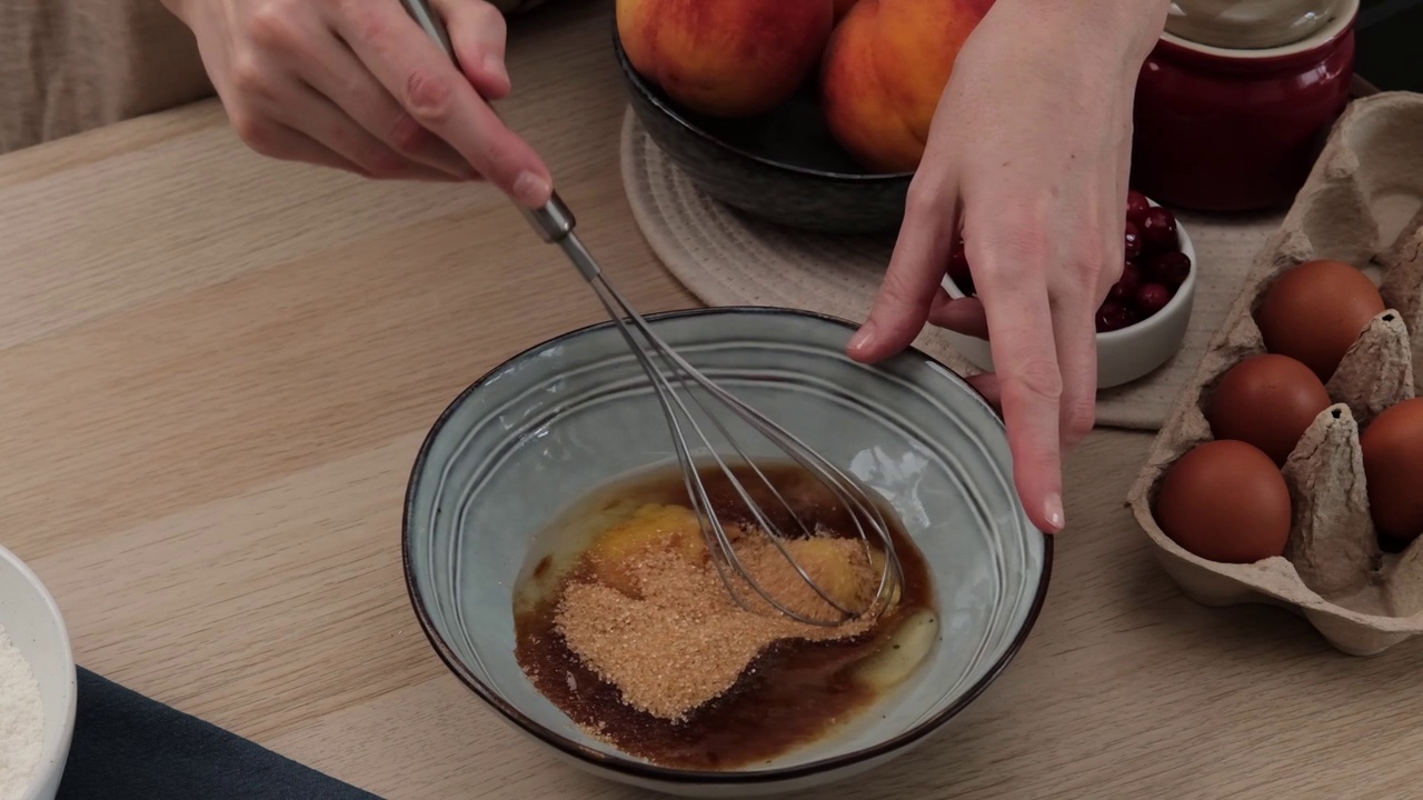 用打蛋器把鸡蛋搅匀。烹饪与配料烘烤的过程。一个女人准备了一个甜酥饼派，里面有桃子和蔓越莓。视频食谱-一步一步烹饪视频下载