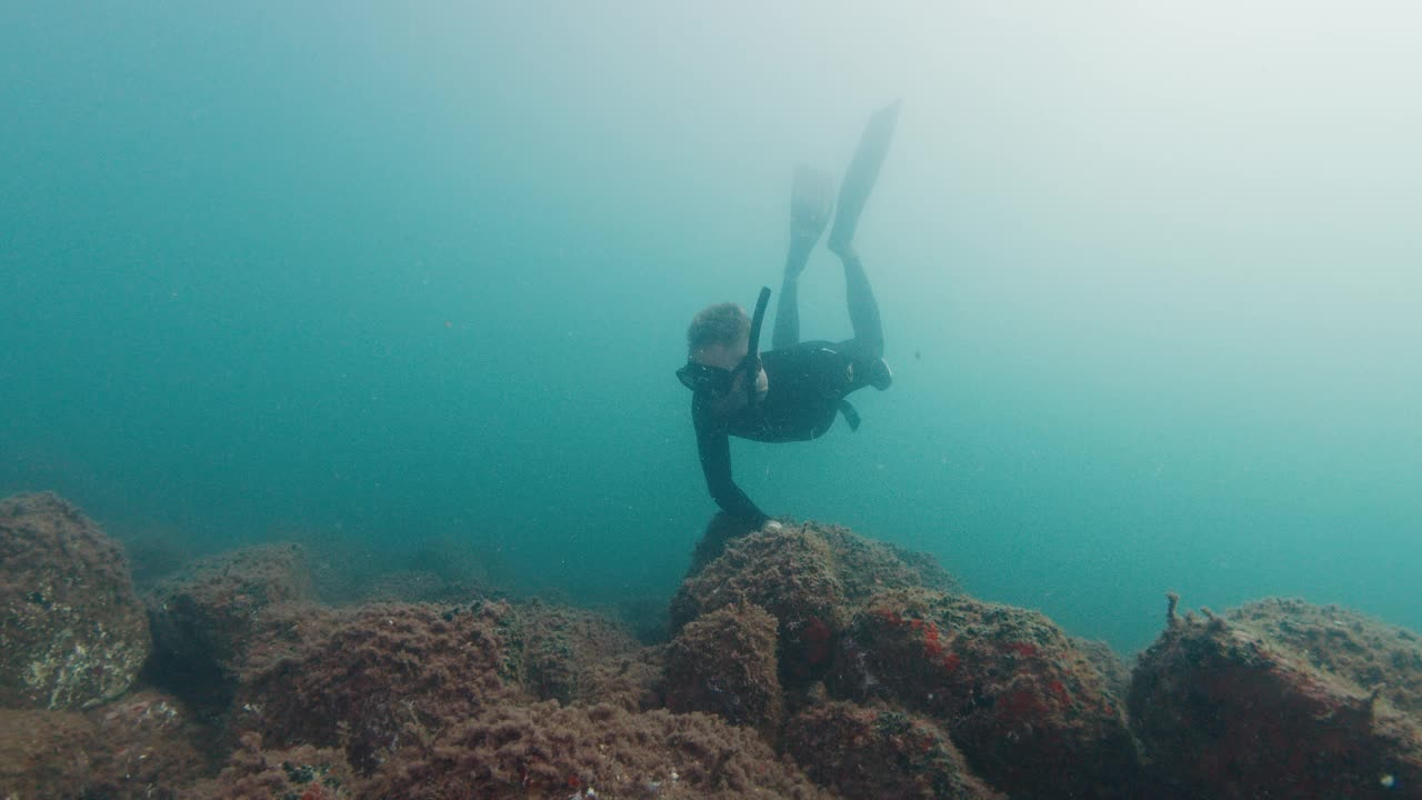 自由潜水者在浑浊的海水中游泳，在岩石底部滑行。在海洋中自由潜水视频素材