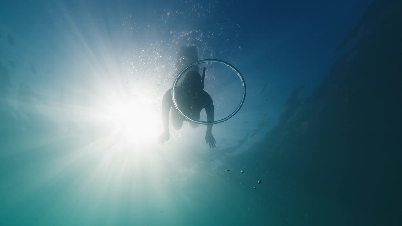 自由潜水员在浑浊的海水中游泳，在环形气泡中滑行。自由潜水员在水下玩环状气泡视频素材