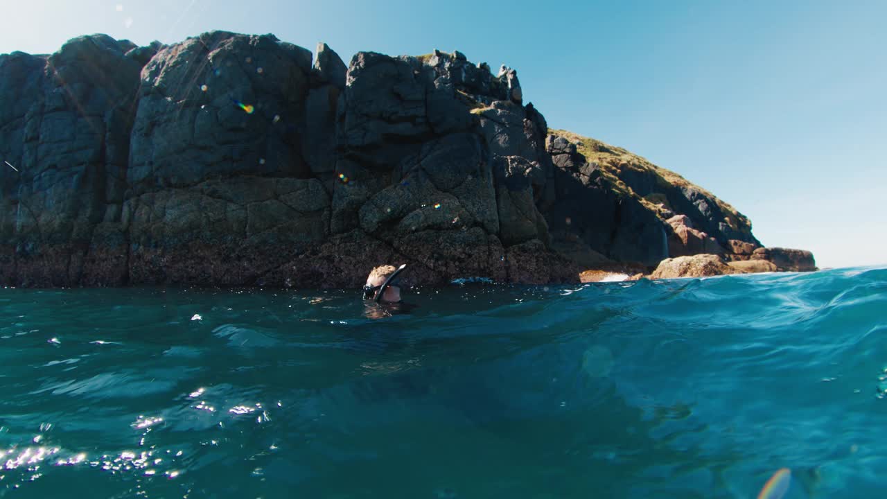 自由潜水者在浑浊的海水中游泳，漂浮在岩石岛附近。自由潜水者在岩石岛附近的海洋中游泳视频素材