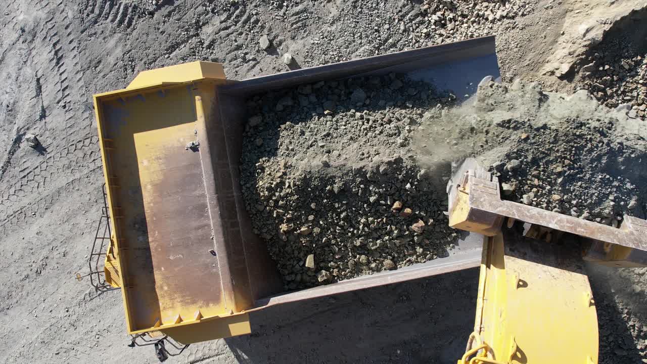 大型斗式挖掘机将矿石装入大型自卸车，露天金矿采掘坑，慢动作航拍视频素材