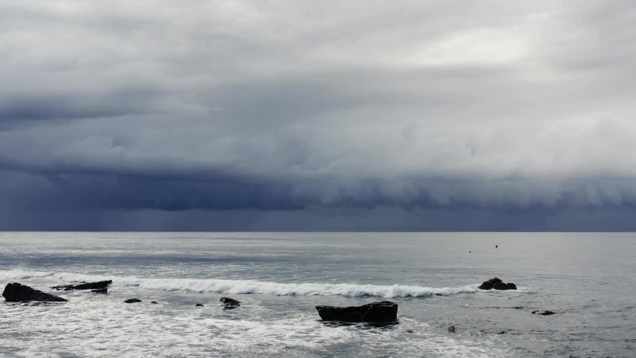 广阔的航拍画面，海浪滚滚涌向海岸，黑暗，戏剧性的风暴云在银色的海洋上移动视频素材