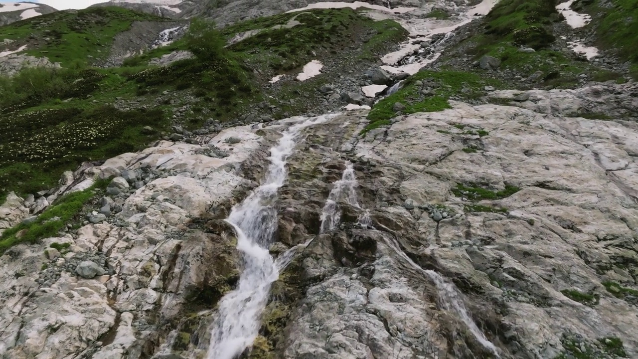 鸟瞰图近距离飞行与山瀑布从冰川流过岩石。瀑布在一个绿色的山峡谷。三轴运动视频素材