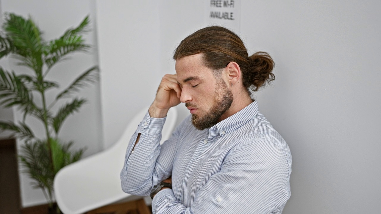 年轻的西班牙裔男子双手交叉坐在椅子上，一脸严肃地站在候诊室里视频素材