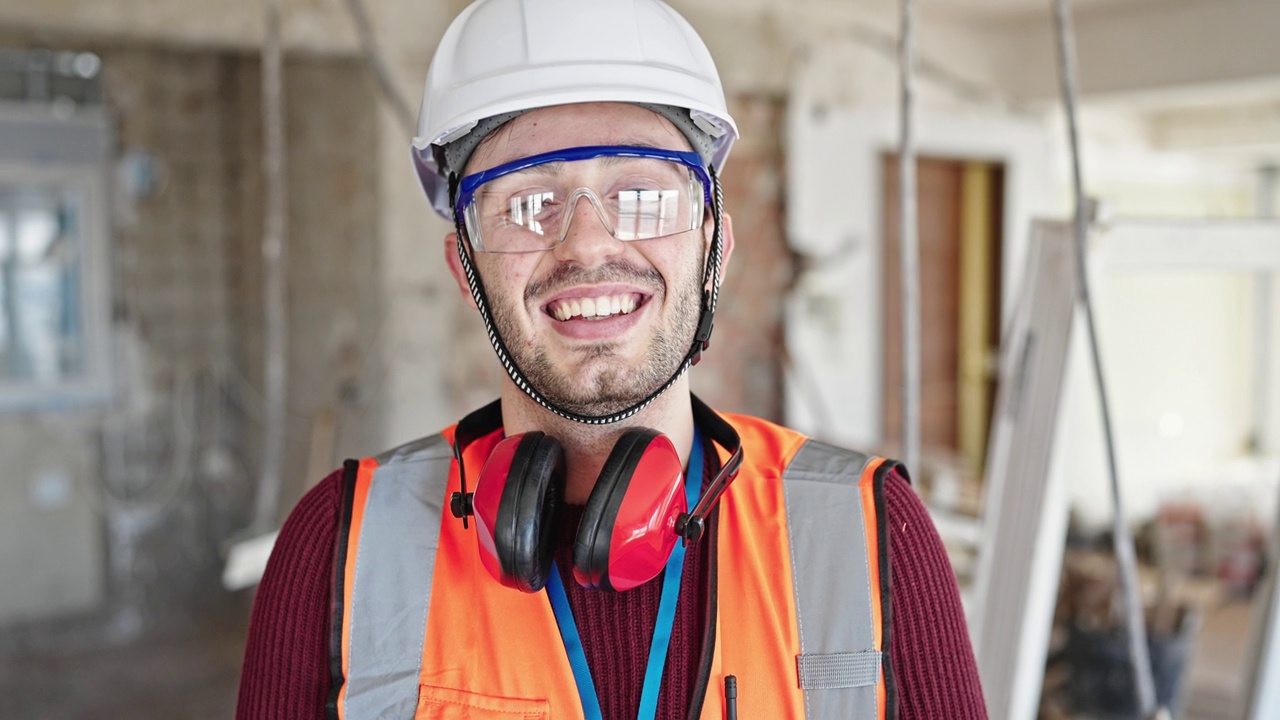 年轻的西班牙裔建筑工人微笑着自信地站在建筑工地视频素材