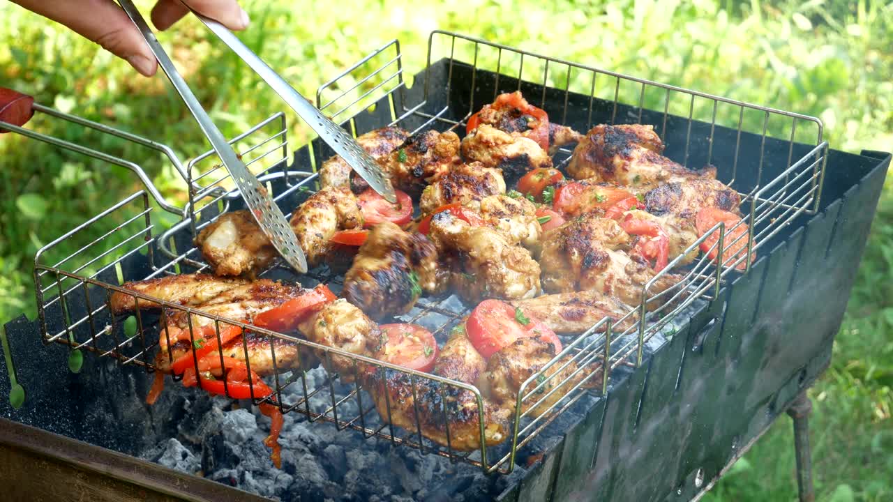 在烤架上烤着。户外烤架上的炸鸡肉和西红柿。视频下载