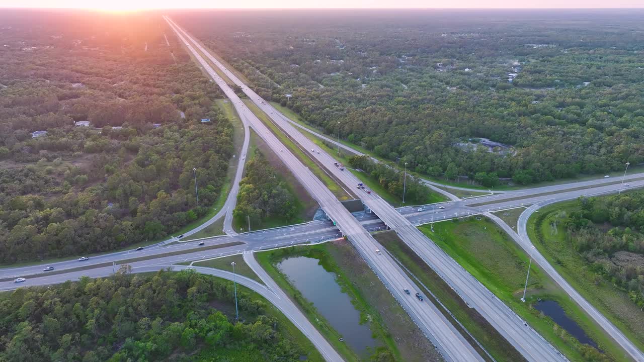 日出时高速公路出口交叉口的高架视图，车道上有快速移动的车辆和卡车。美国州际交通基础设施视频素材