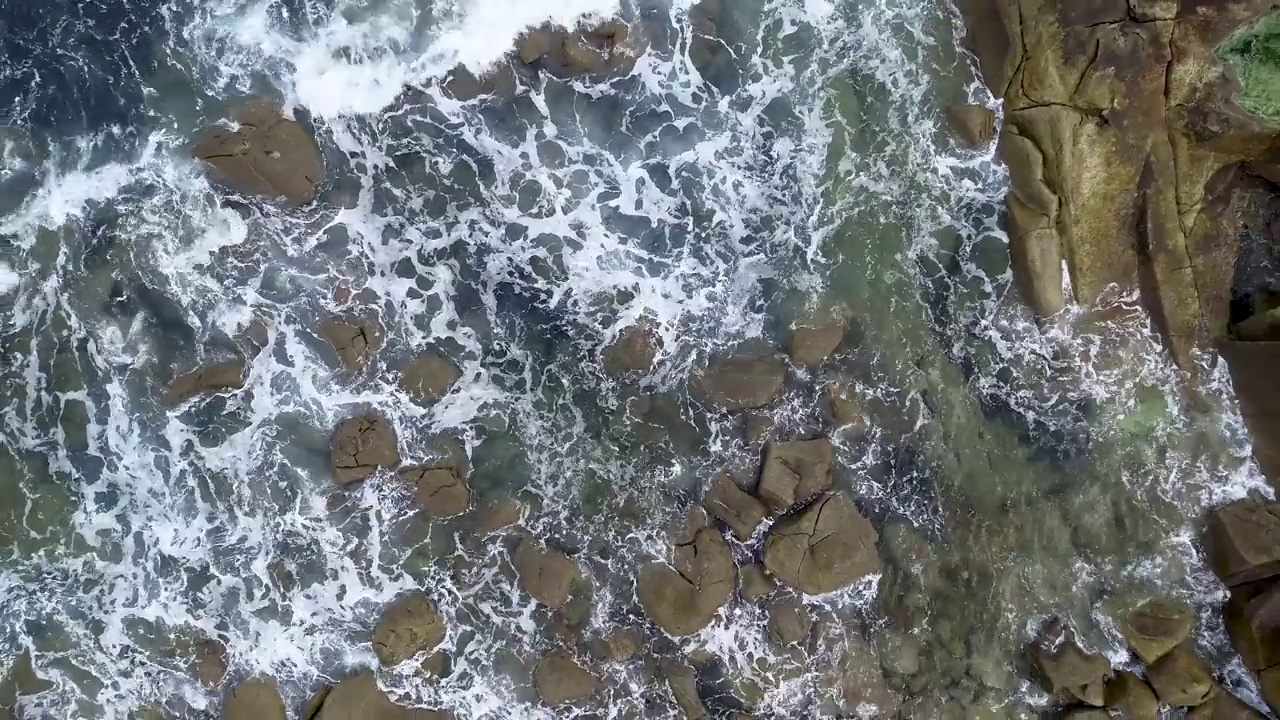 无人机飞过海浪，撞击着海滩上的岩石视频素材