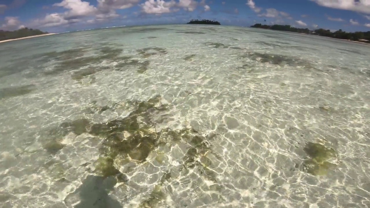 宽阔的视角，在清澈的蓝绿色浅海湖咸水和沙滩的海底与珊瑚礁和涟漪的反射看向地平线向高冈岛的一天视频素材