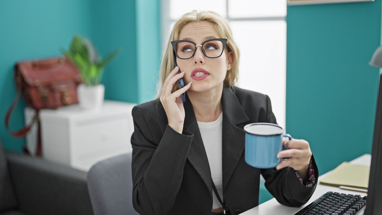 年轻的金发女商务人员在办公室用智能手机聊天，喝咖啡视频素材