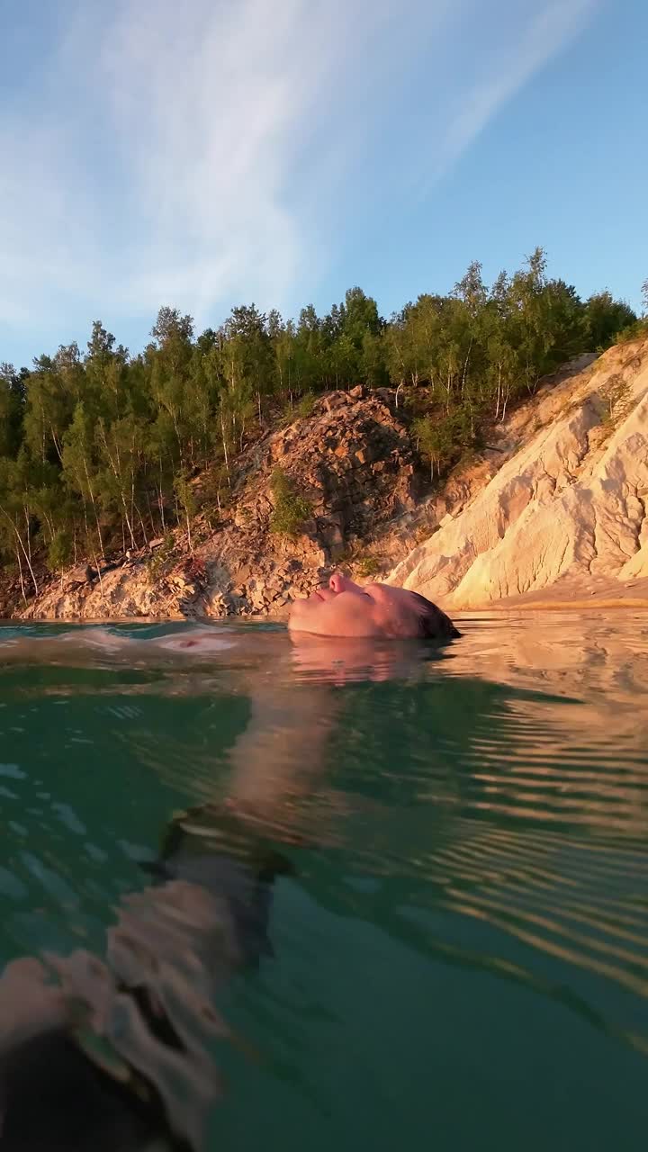 在一个初夏的早晨，一名男子仰面漂浮在风景如画的风景上。垂直视频视频素材